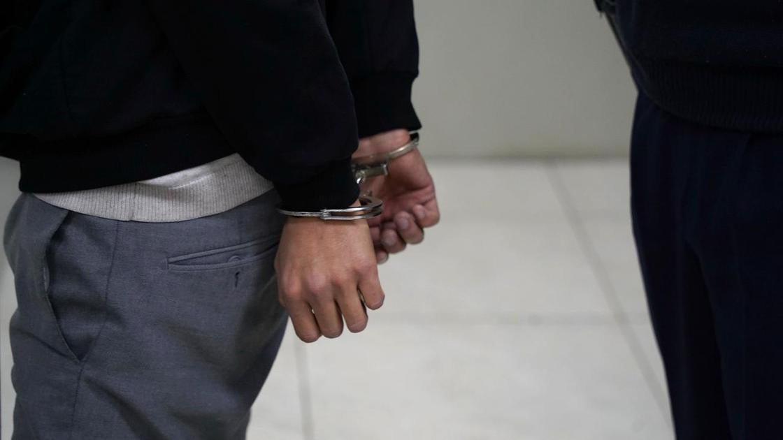 Мужчина в наручниках стоит в коридоре отделения полиции
