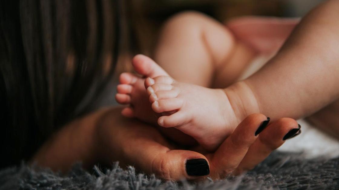 Женская рука держит ноги младенца