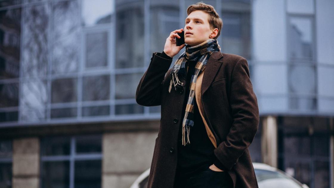 Мужчина в стильном пальто и шарфе разговаривает по телефону
