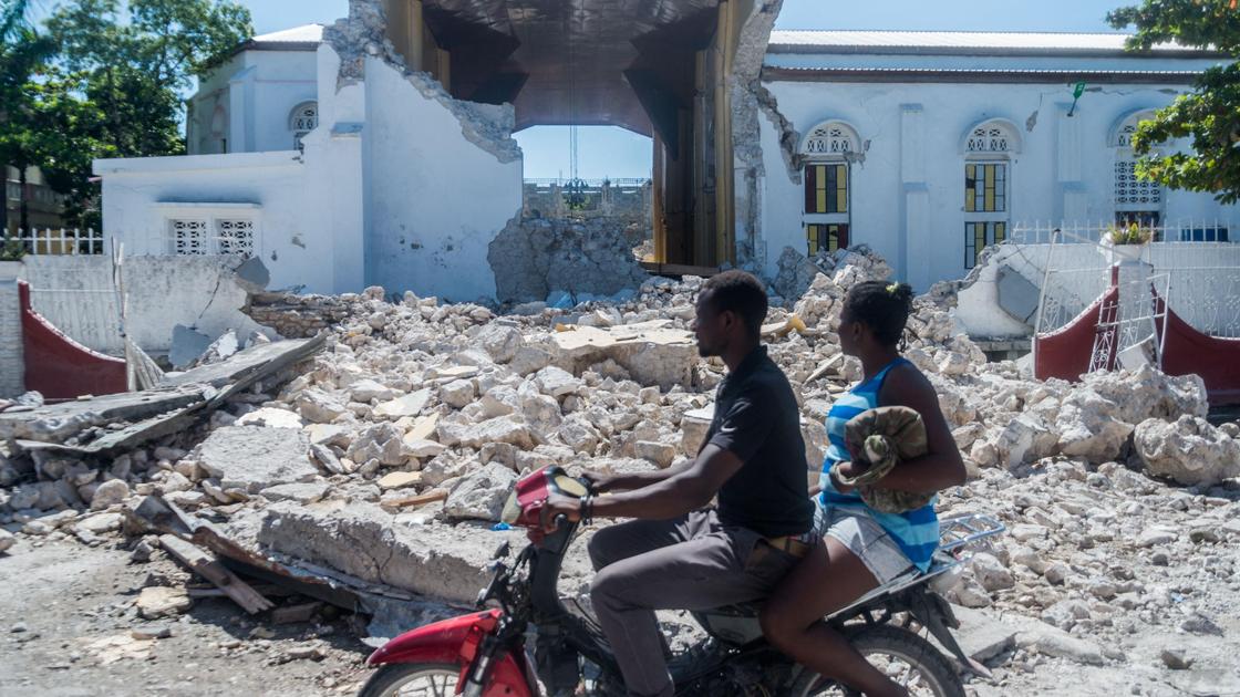 Жители Гаити проезжают около разрушенных зданий