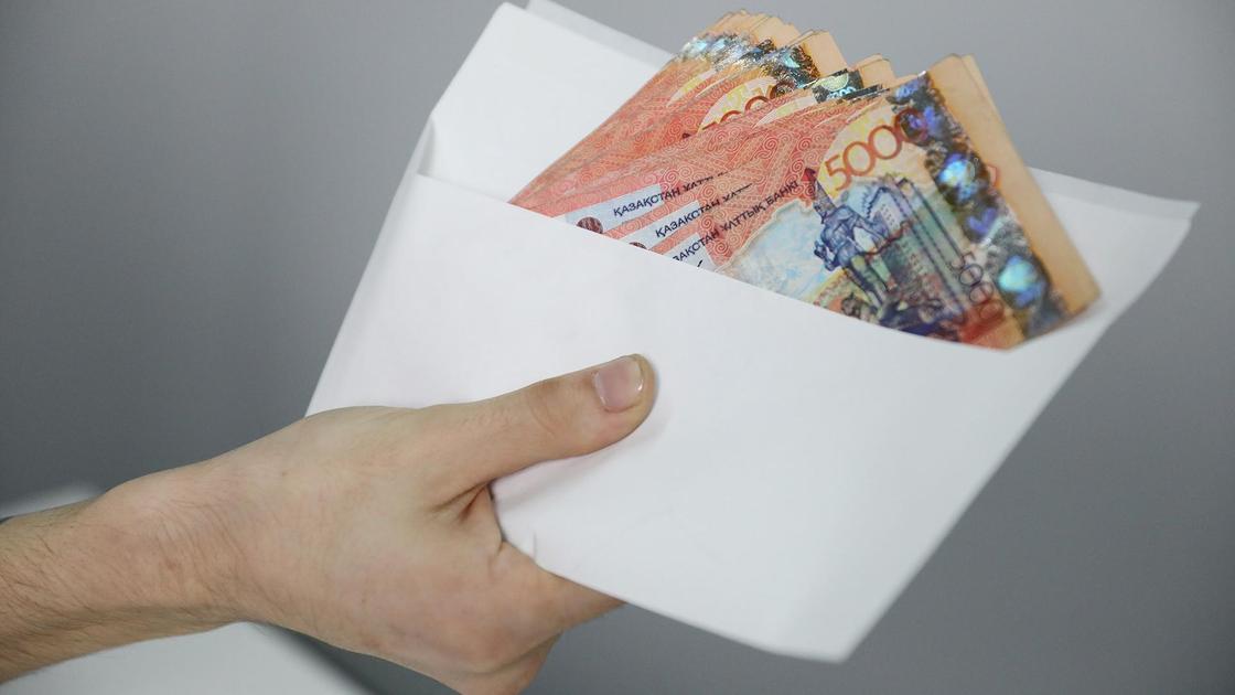 Рука держит конверт с 5000-ными купюрами в тенге