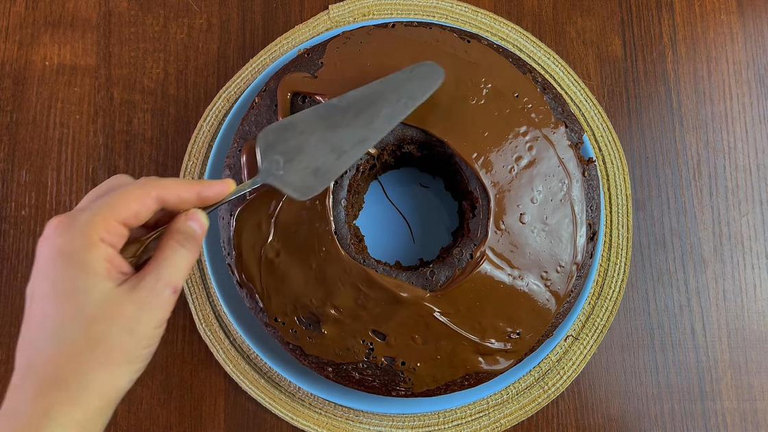 На тарелке пирог, который покрывают растопленным шоколадом