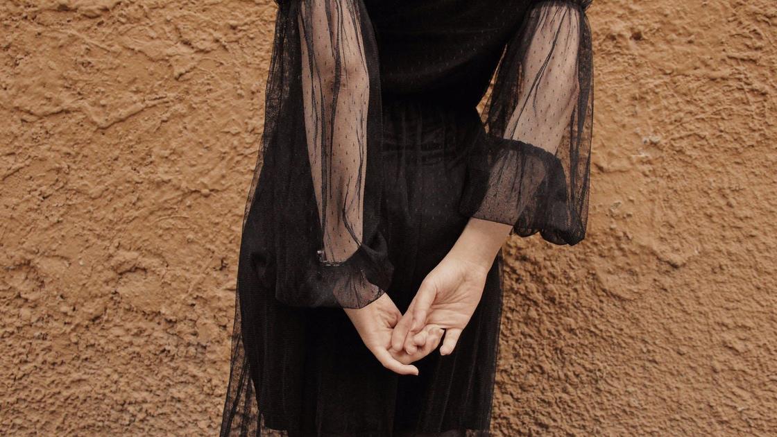 Девушка в черном платье стоит у стены