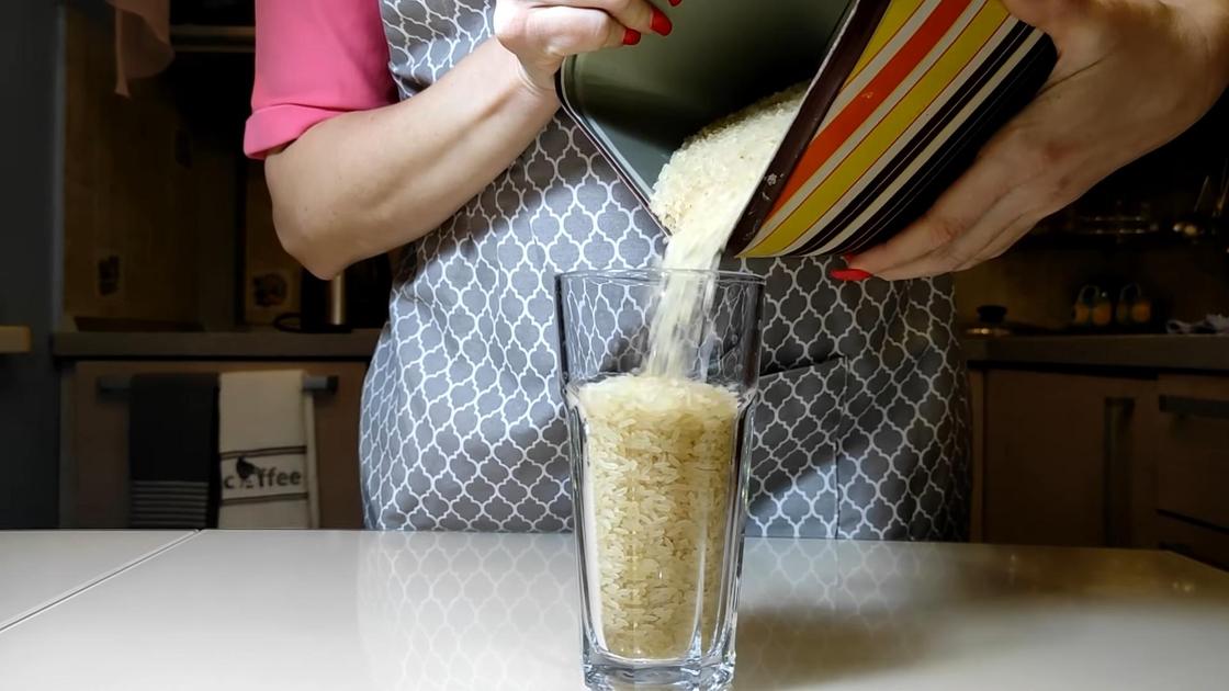 Женщина насыпает рис в стакан из емкости для сыпучих