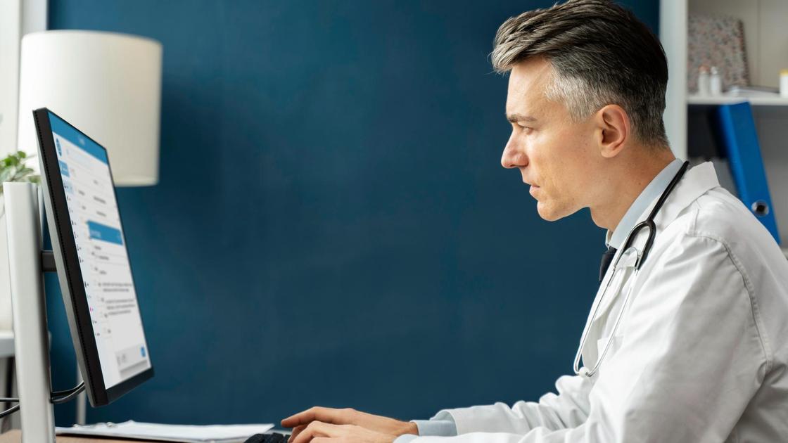 Мужчина в белом халате сидит за компьютером
