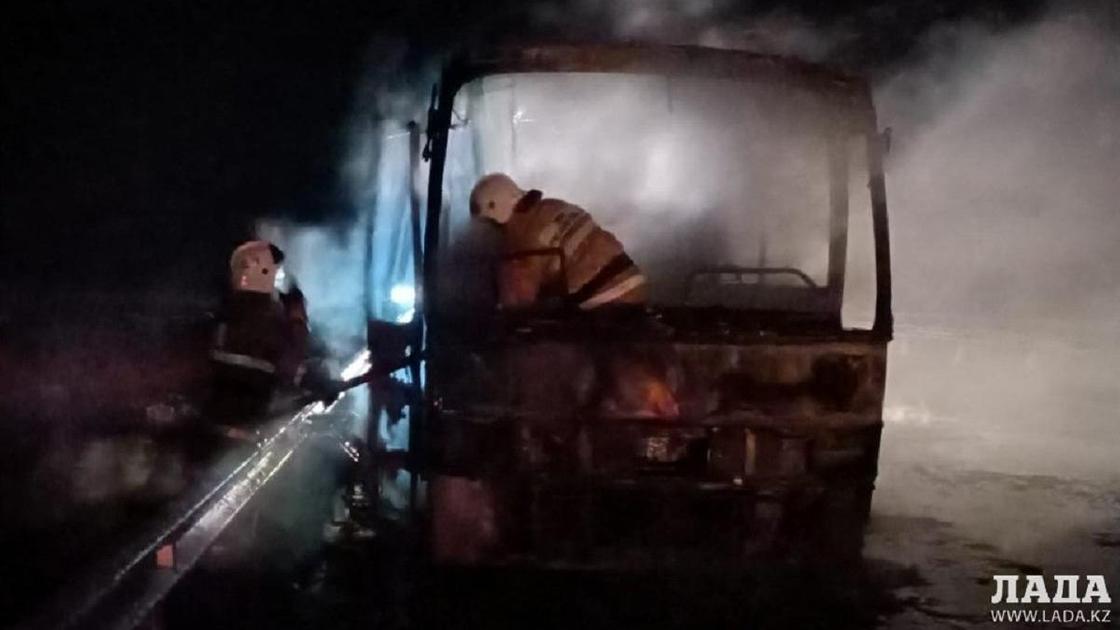 Двое пожарных среди дыма от сгоревшего автобуса
