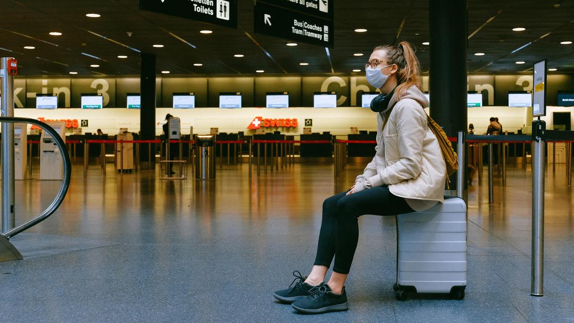 Девушка сидит на чемодане в аэропорту