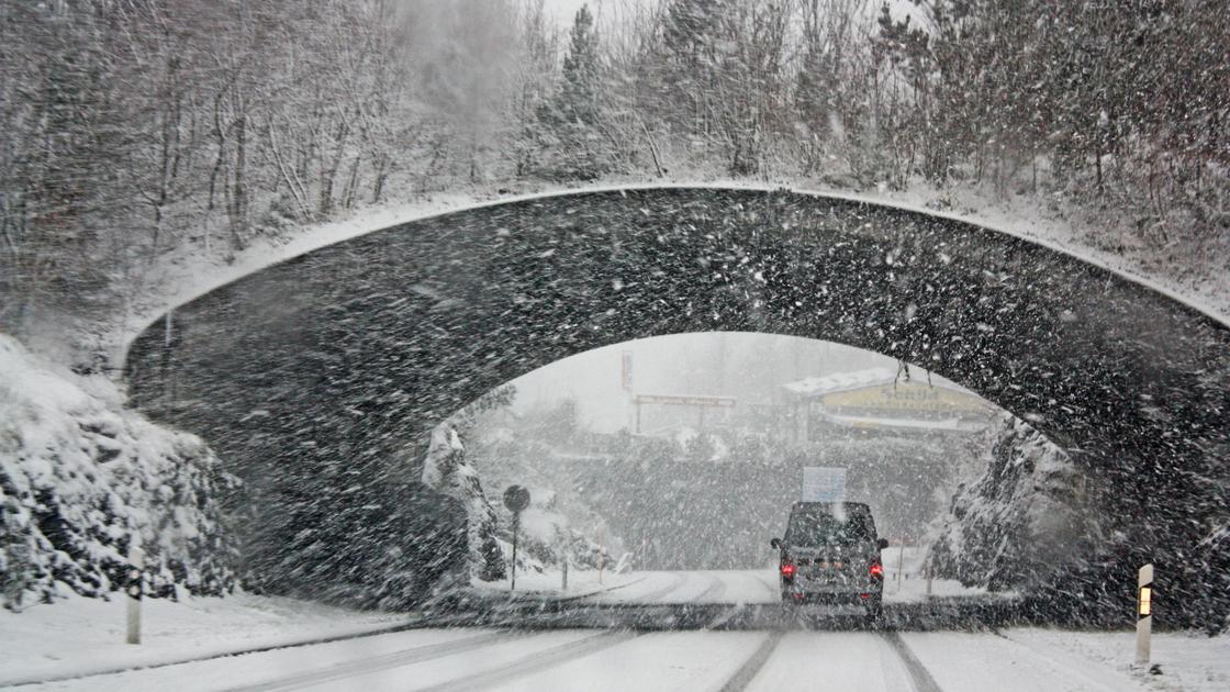 Машина едет по дороге в сильный снег