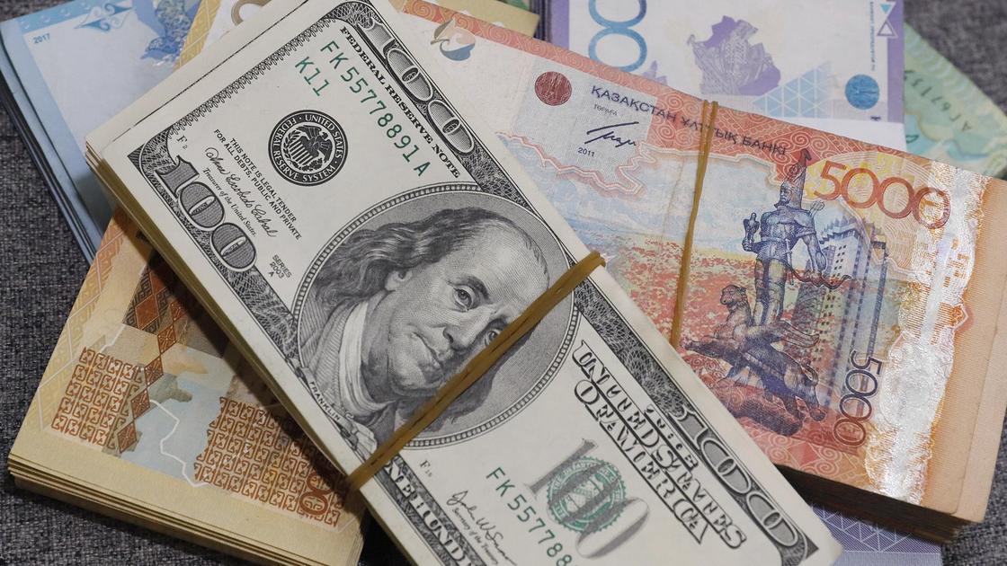 Пачка долларов лежит среди пачек тенге