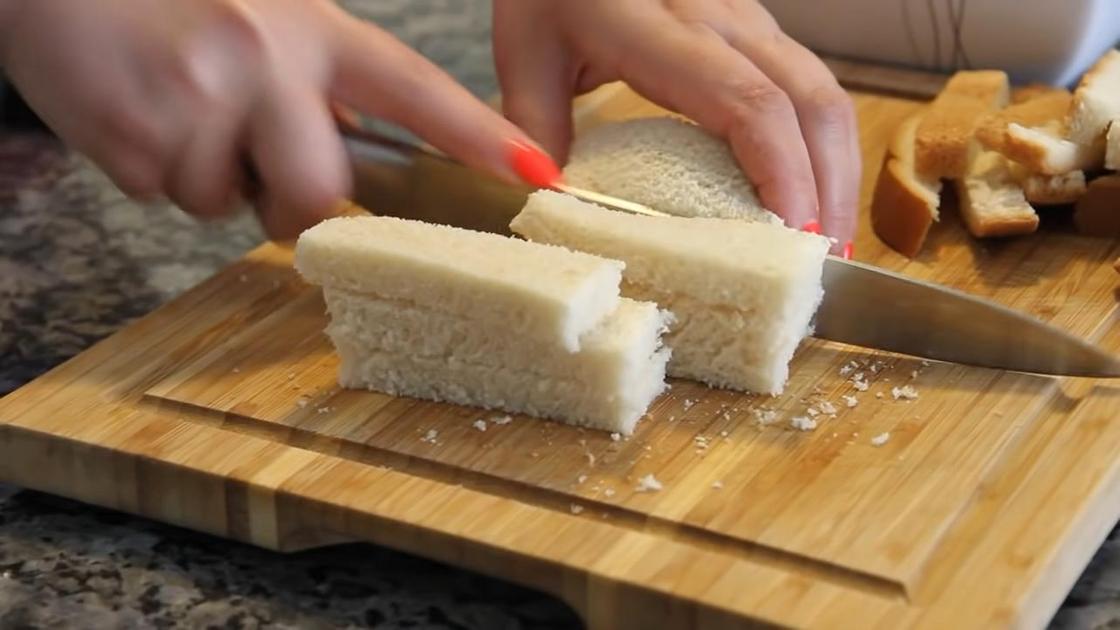 Девушка нарезает белый хлеб дольками на разделочной доске