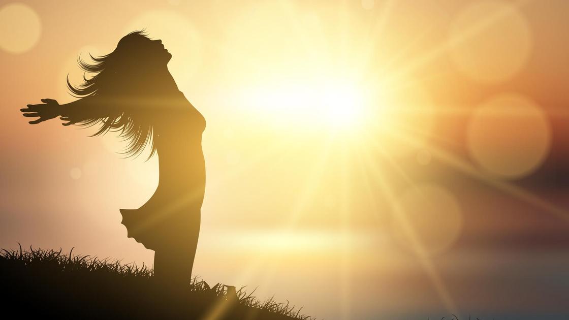 Фигура женщины с раскрытыми руками на фоне солнца