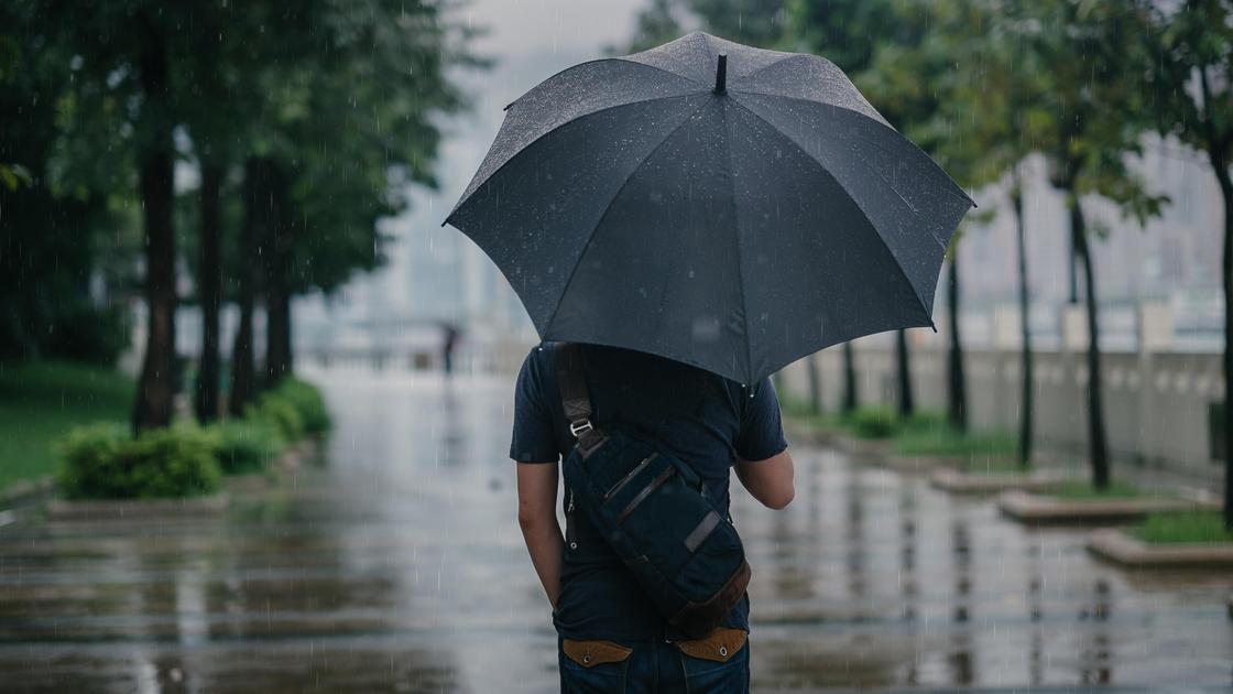 Мужчина идет по городу с зонтом во время дождя