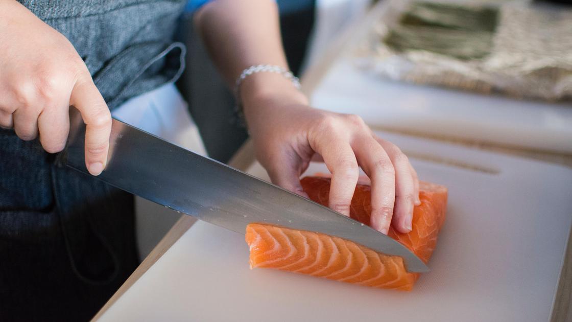 Женщина режет ножом рыбу