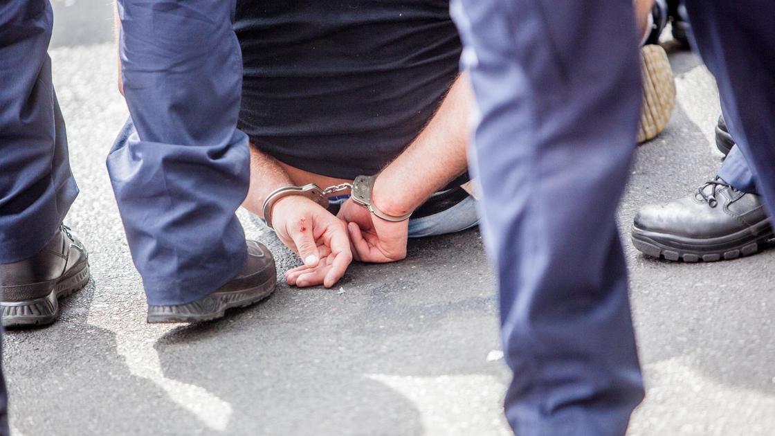 Мужчина сидит на земле в наручниках в окружении других людей