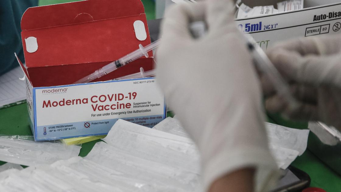 Человек держит шприц в руках на фоне коробки с вакциной Moderna