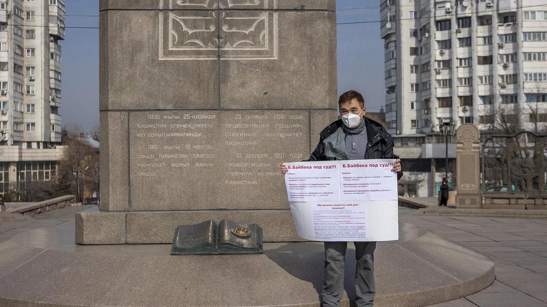 Мужчина стоит с плакатом возле монумента