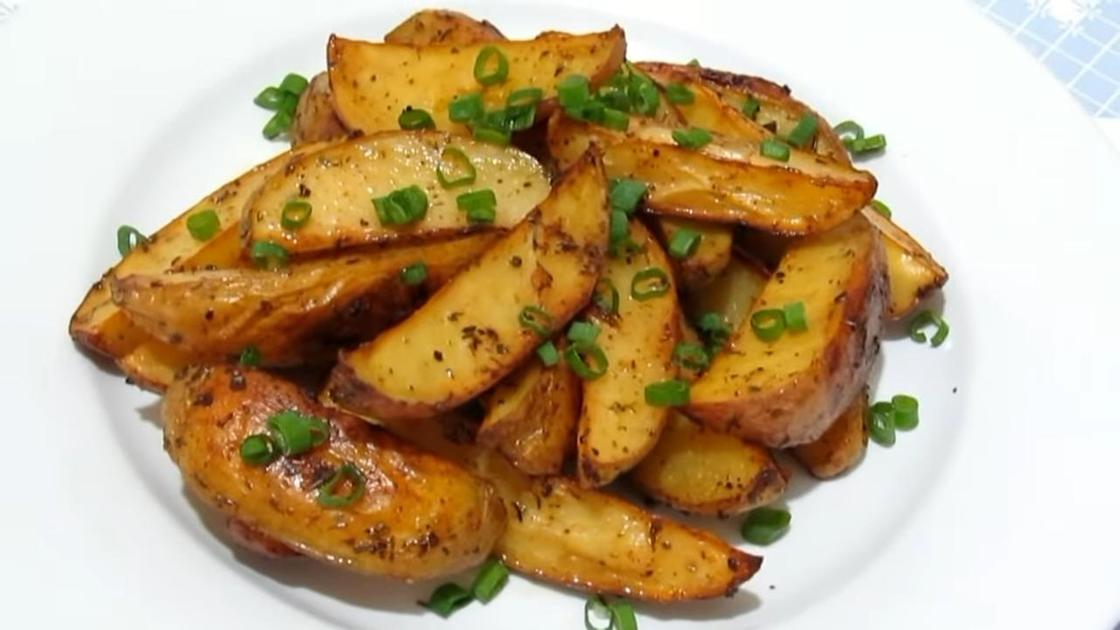 Запеченный картофель по-деревенски на тарелке, посыпанный зеленым луком