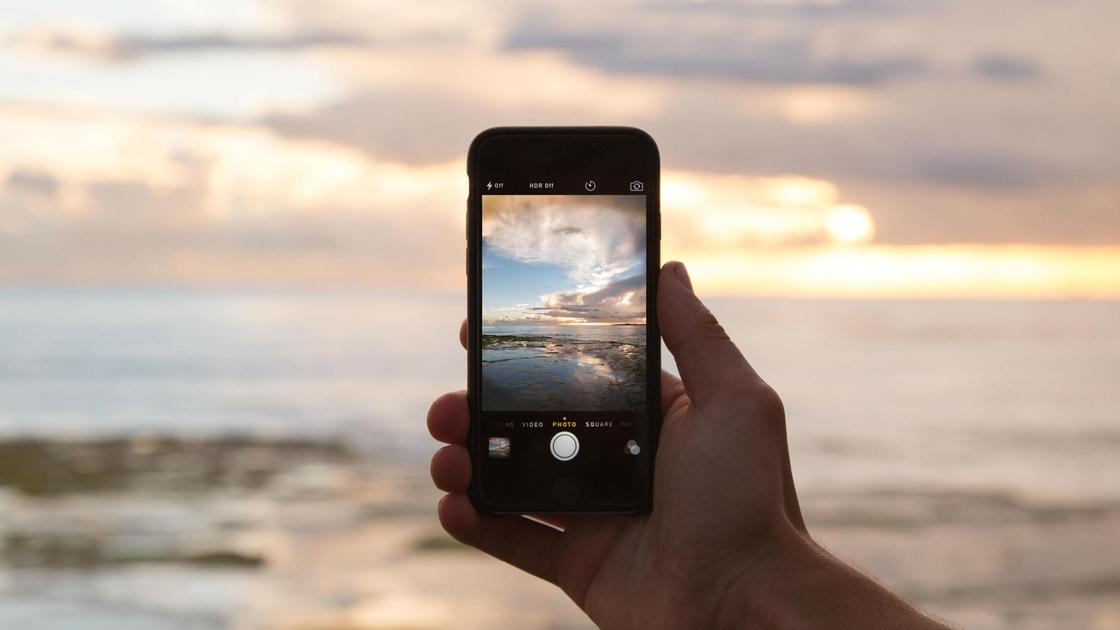 Человек фотографирует закат на смартфон