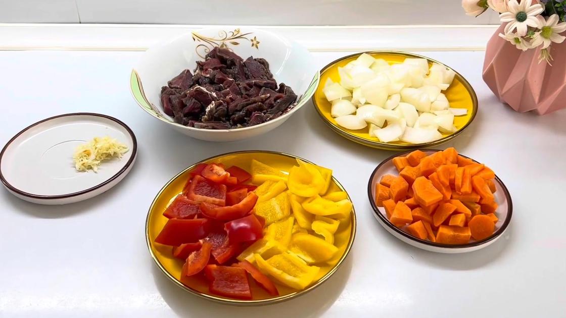 На столе тарелки с нарезанными ингредиентами: говядиной, луком, морковью, перцем