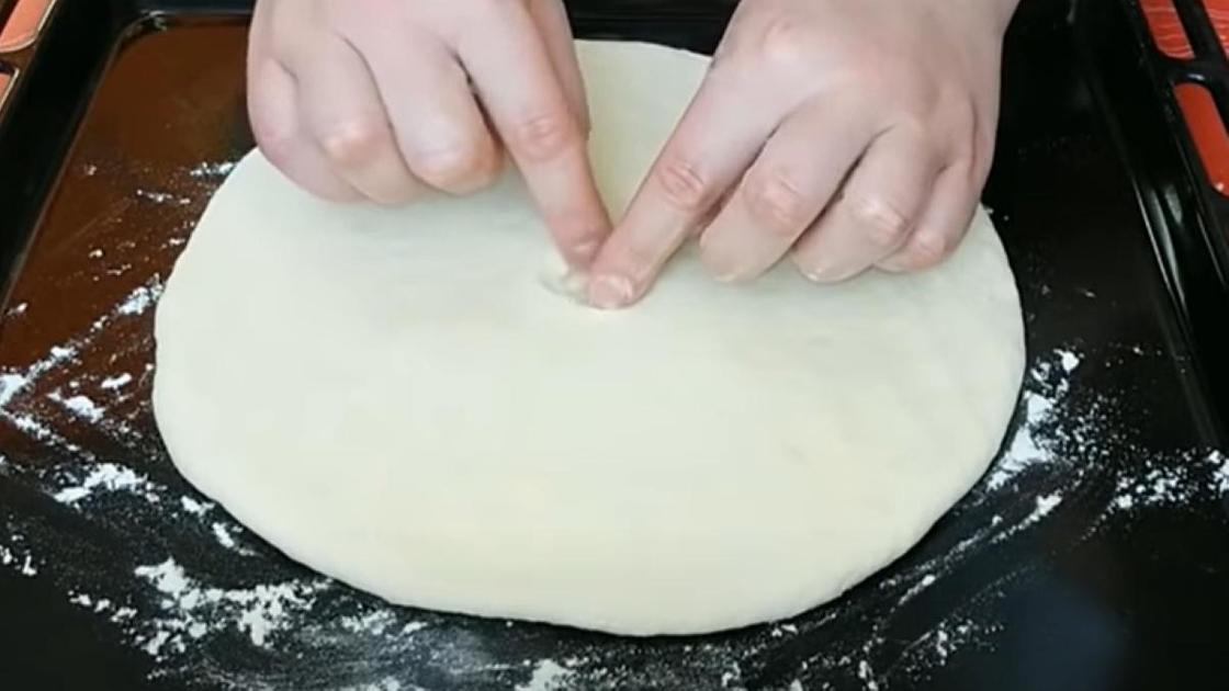 Руками по центру плоского пирога на противне делают небольшое отверстие