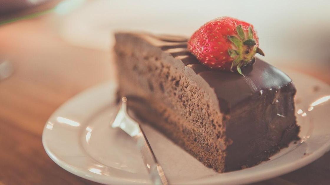 Кусочек шоколадного торта, украшенного клубничкой, на тарелке