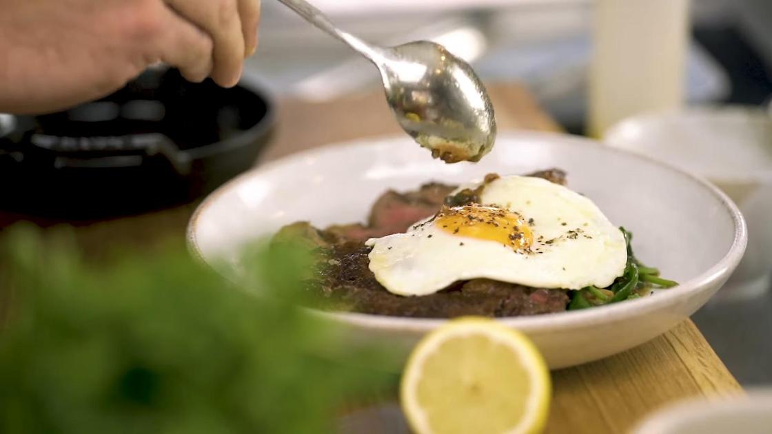 На сервировочной тарелке шпинат, нарезанный стейк и жаренное яйцо