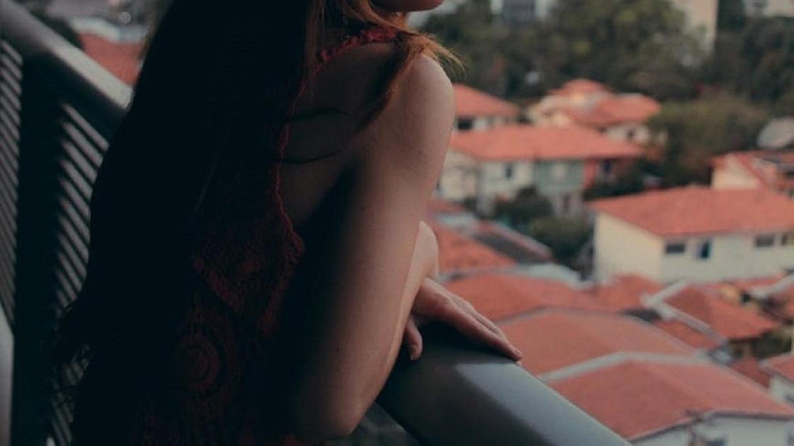 Девушка стоит на балконе и смотрит на город