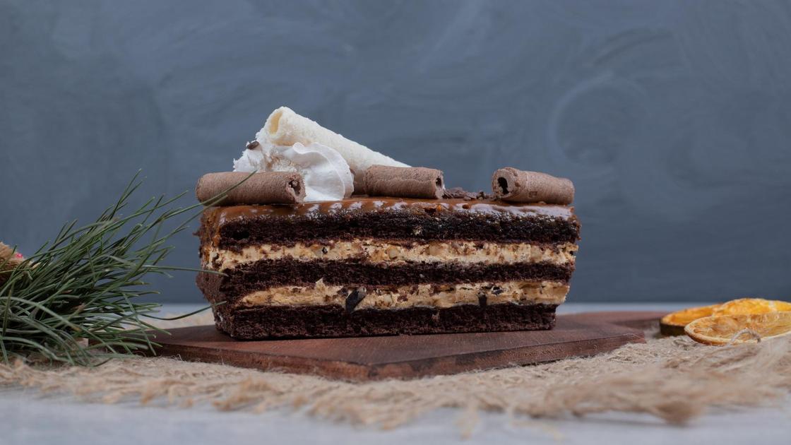 Кусочек шоколадного торта с масляным кремом и шоколадной помадкой, декорированный палочками корицы