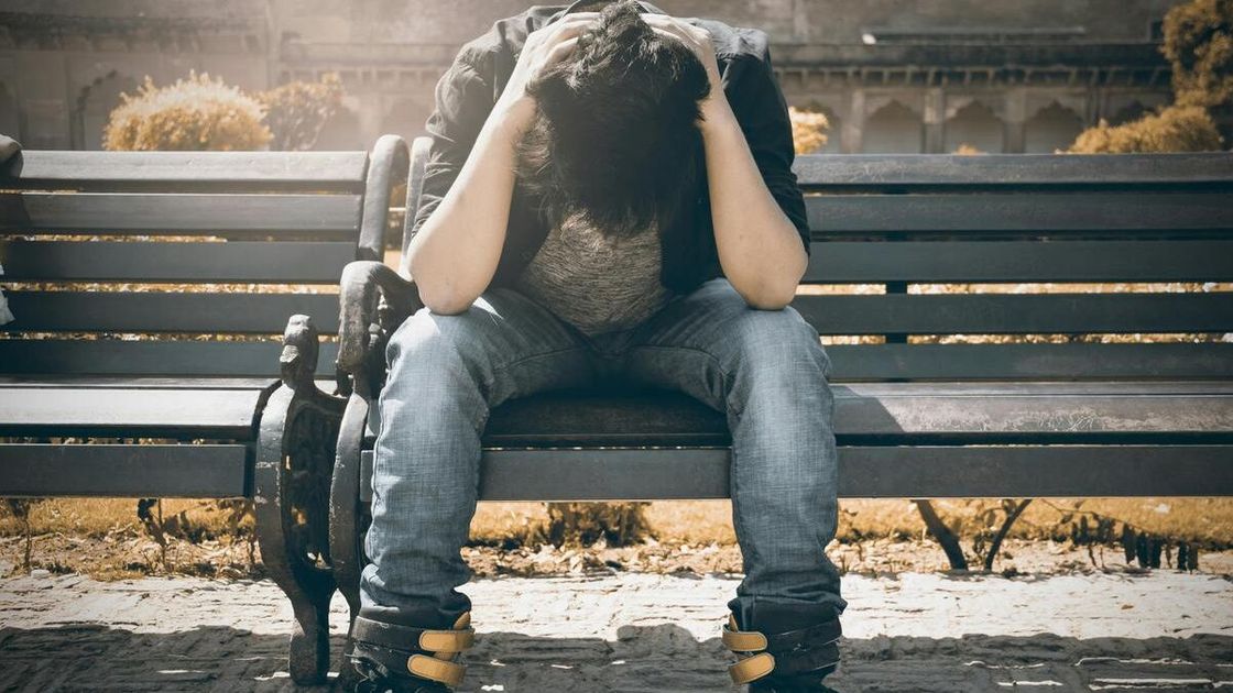 Парень держится за голову, сидя на лавочке