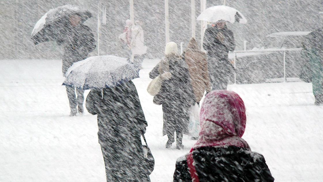 Люди идут с зонтами по улице во время сильного снегопада