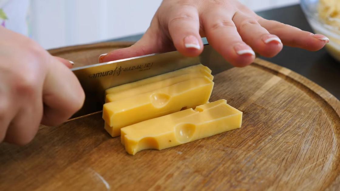 Твердый сыр нарезают на разделочной доске