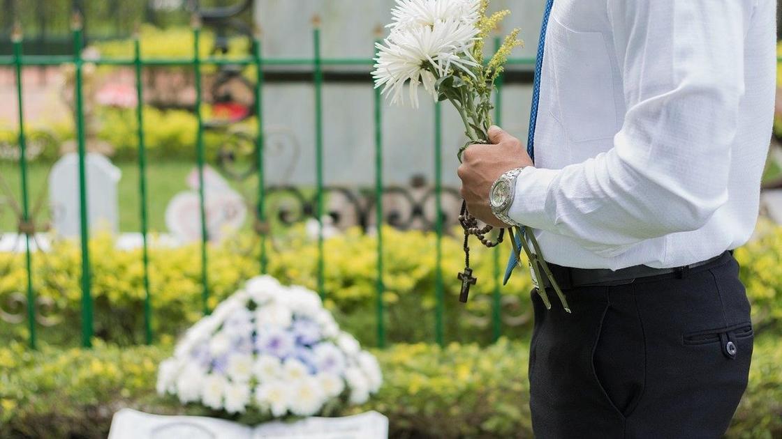 мужчина с цветами стоит на кладбище