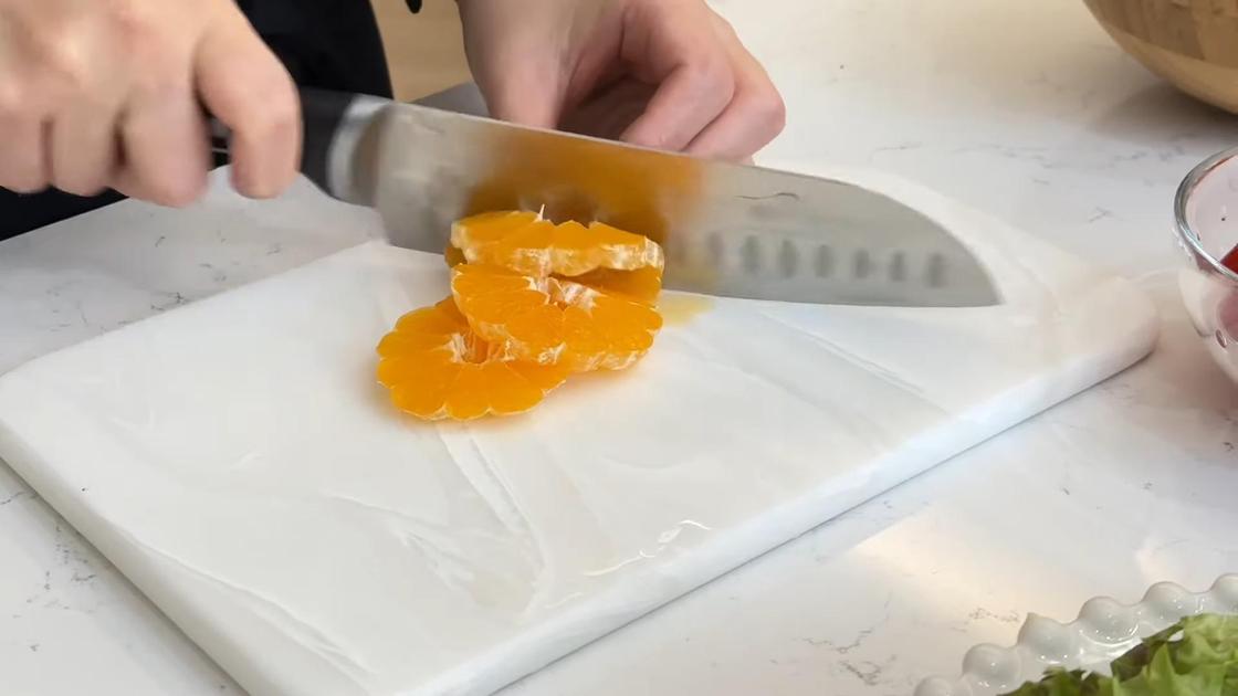 На разделочной доске нарезают очищенный апельсин