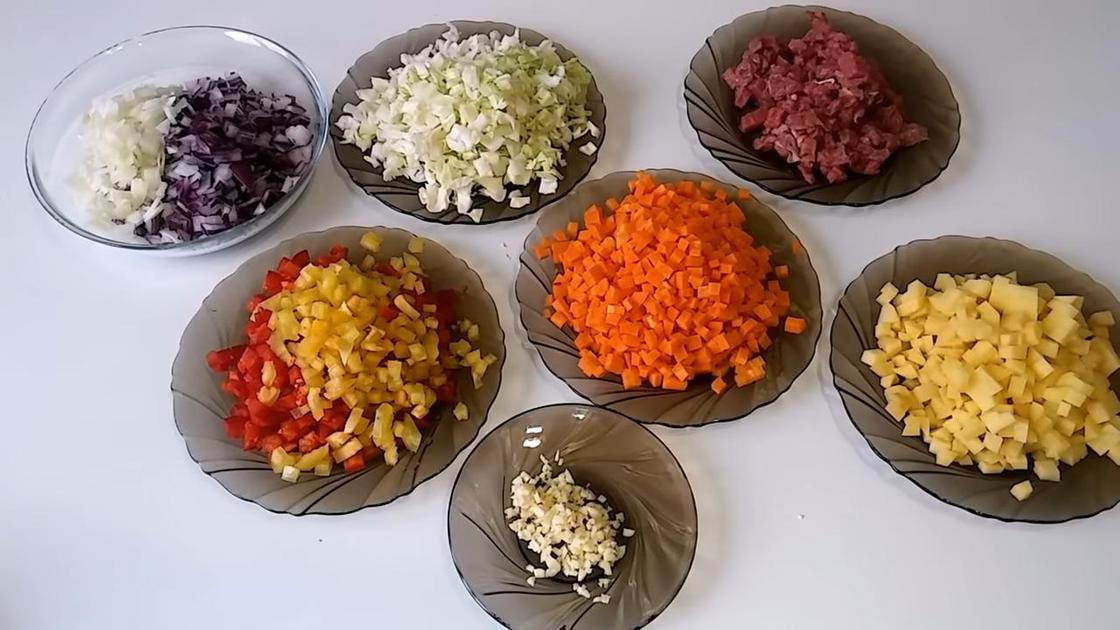 В тарелках нарезанные овощи: морковь, капуста, картофель, лук, перец. Также нарезанная говядина