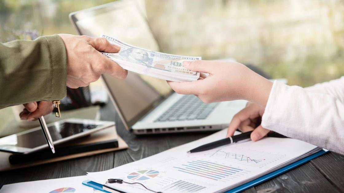 Одна рука передает другой долларовые купюры