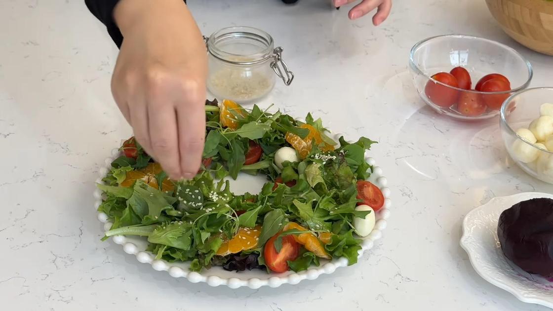 Салат из салатных листьев, помидоров и сыра посыпают кунжутом