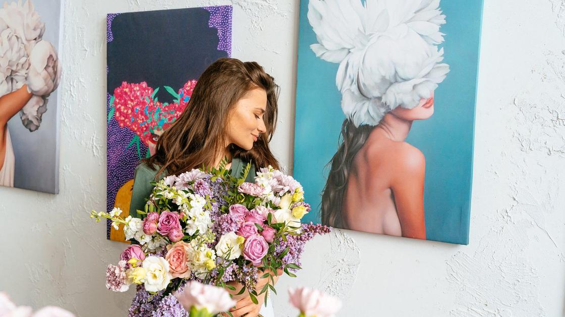 Девушка с букетом цветов на фоне висящей на стене современной живописи