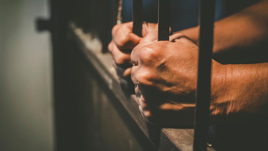 Мужчина сжимает прутья решетки внутри тюремной камеры