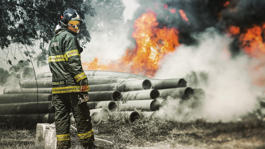 Пожарный стоит возле горящих труб