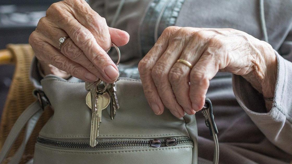 Пожилая женщина держит в руках сумочку и ключи