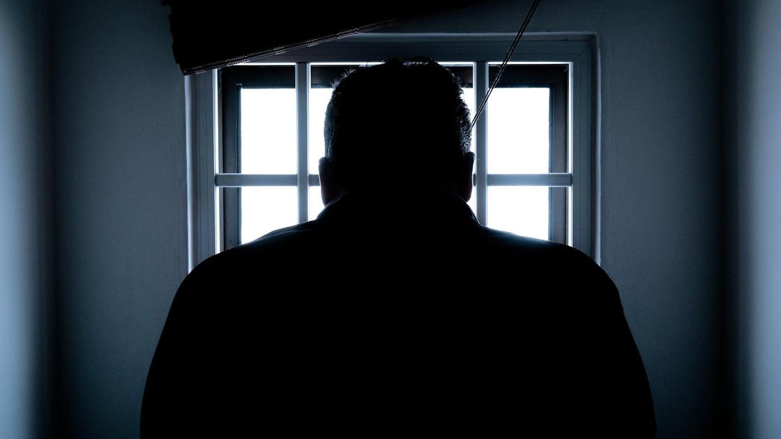 Мужчина стоит возле окна в тюрьме