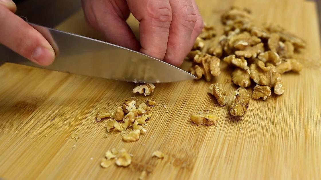Грецкие орехи нарезают ножом на разделочной доске