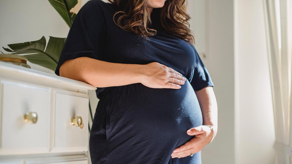 Беременная женщина стоит у комода