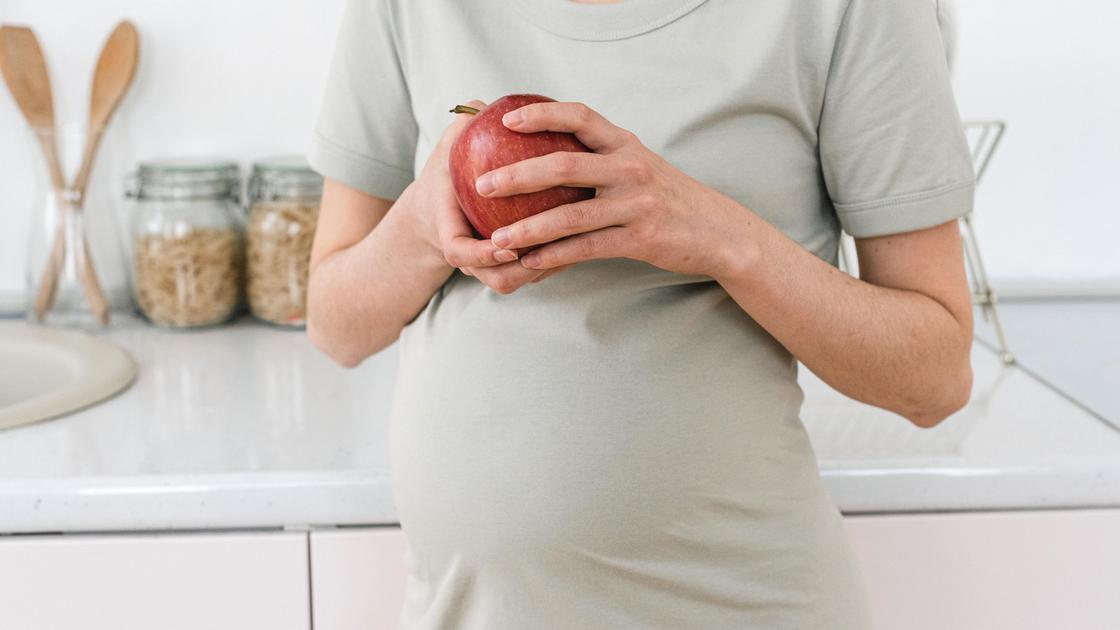 Беременная девушка держит в руках яблоко