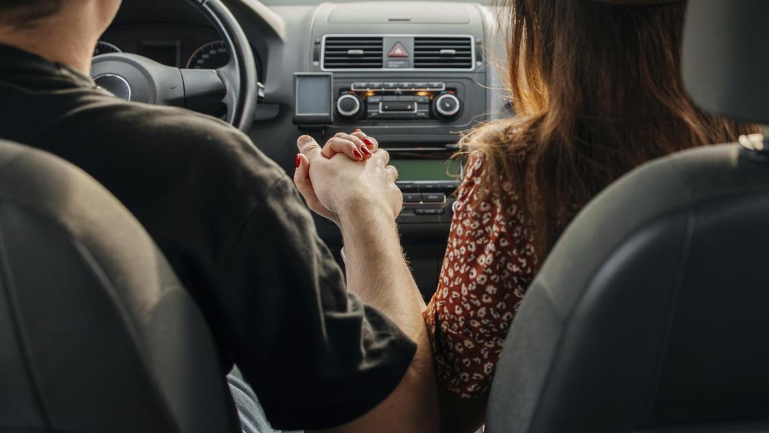 Мужчина и женщина в автомобиле держатся за руки