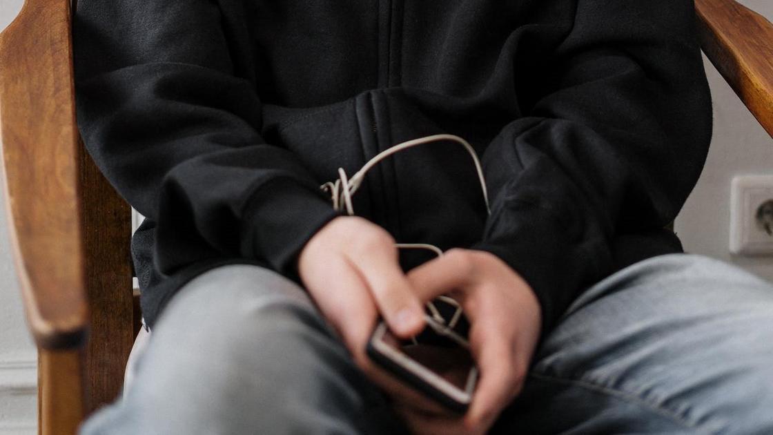 Мальчик-подросток держит в руках телефон с наушниками