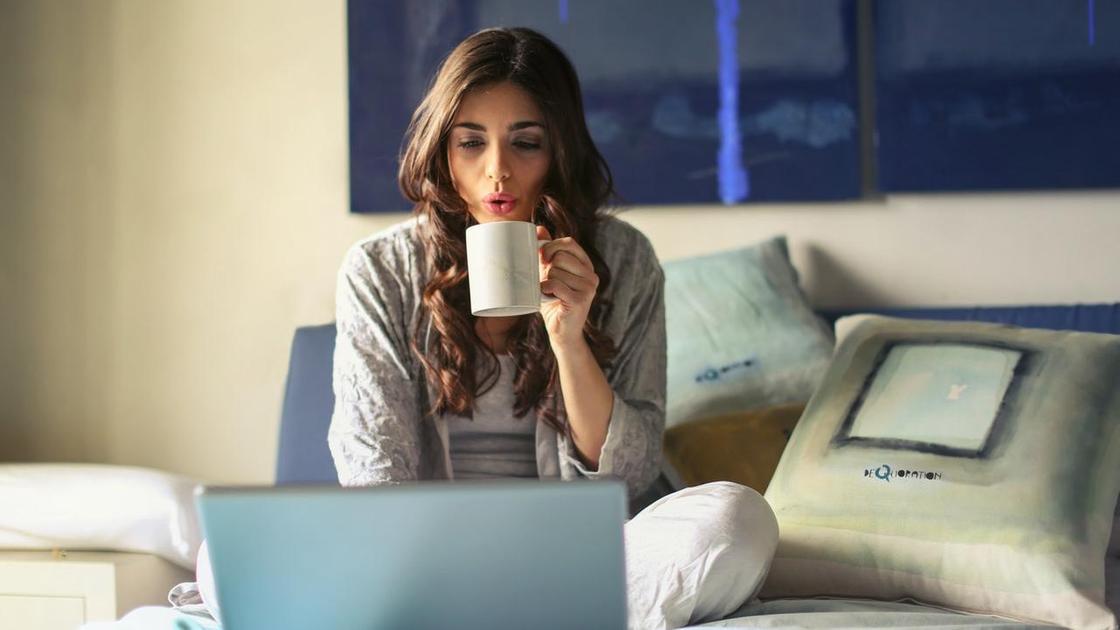 девушка держит чашку и смотрит на экран ноутбука