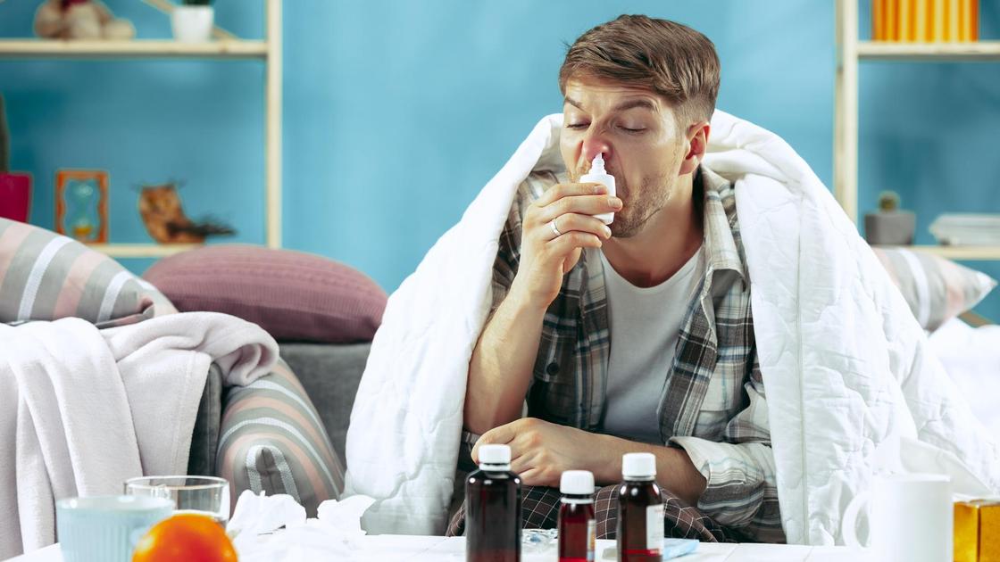 Заболевший мужчина брызгает назальный спрей в нос