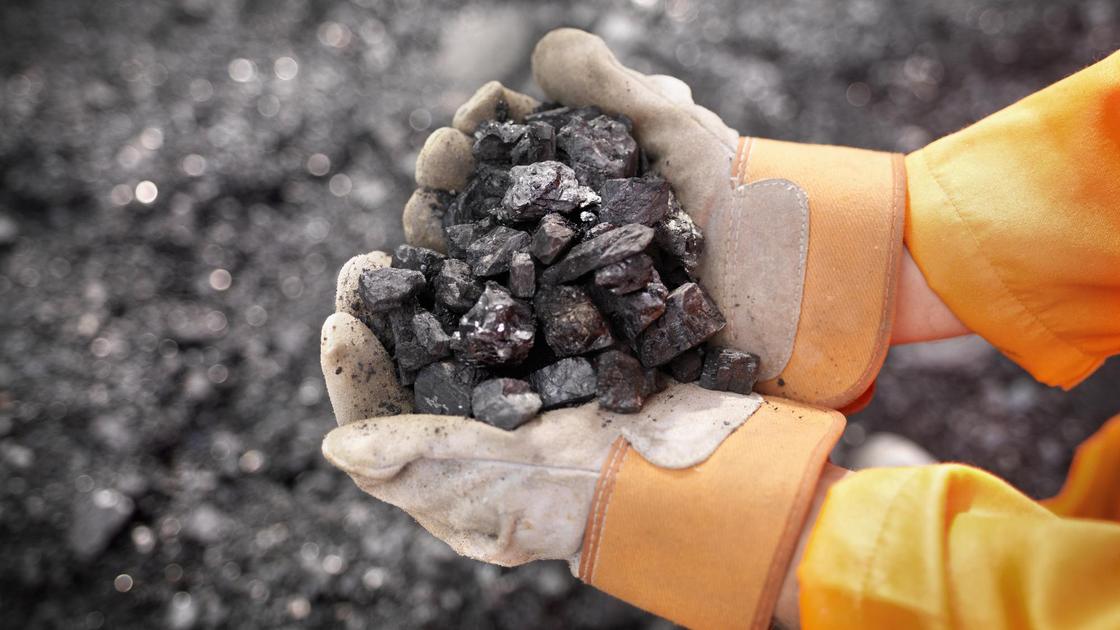Рабочий в перчатках держит уголь