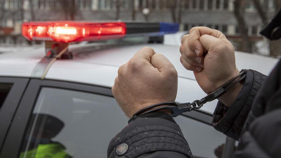 Мужчина в наручниках стоит возле полицейского авто